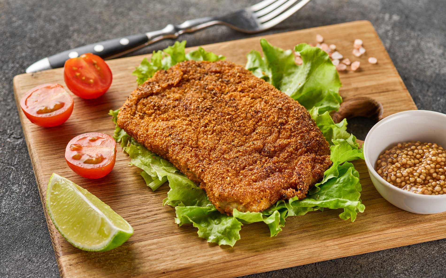 A schnitzel on a cutting board with lemon and cherry tomatoes