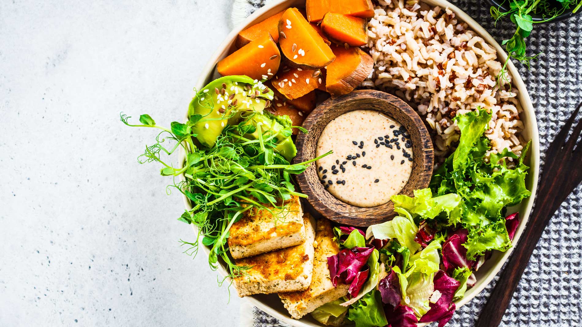 Buddha bowl with tofu, avocado, rice, seedlings, sweet potato, and tahini dressing.