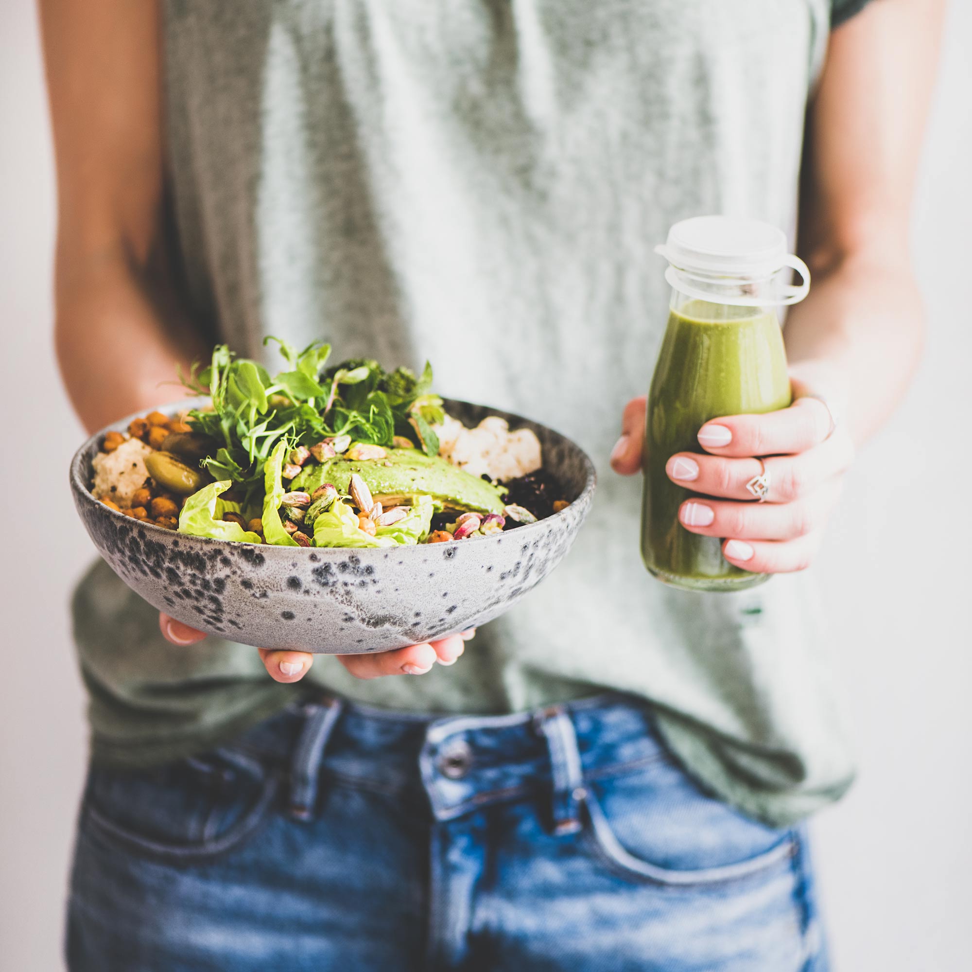 woman holding a bowl of salad and a green smoothie