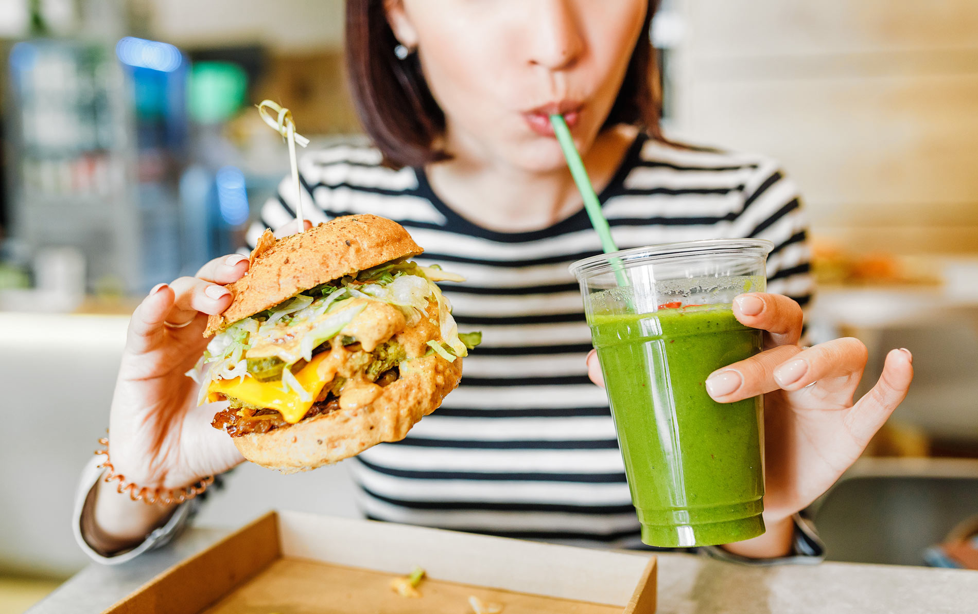 woman holding a vegan burger and a green smoothie