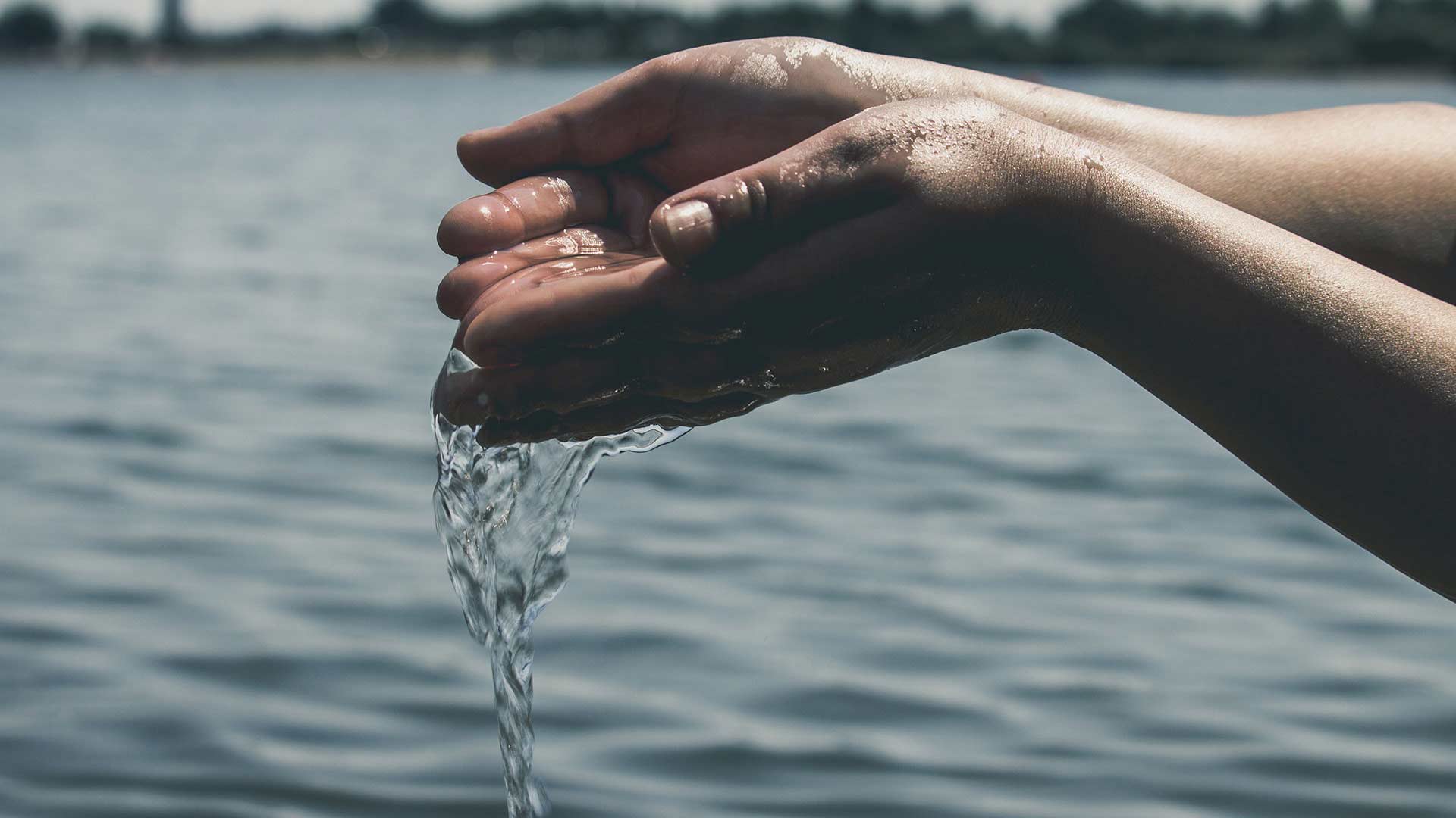 hands put together holding water and the sea in the background