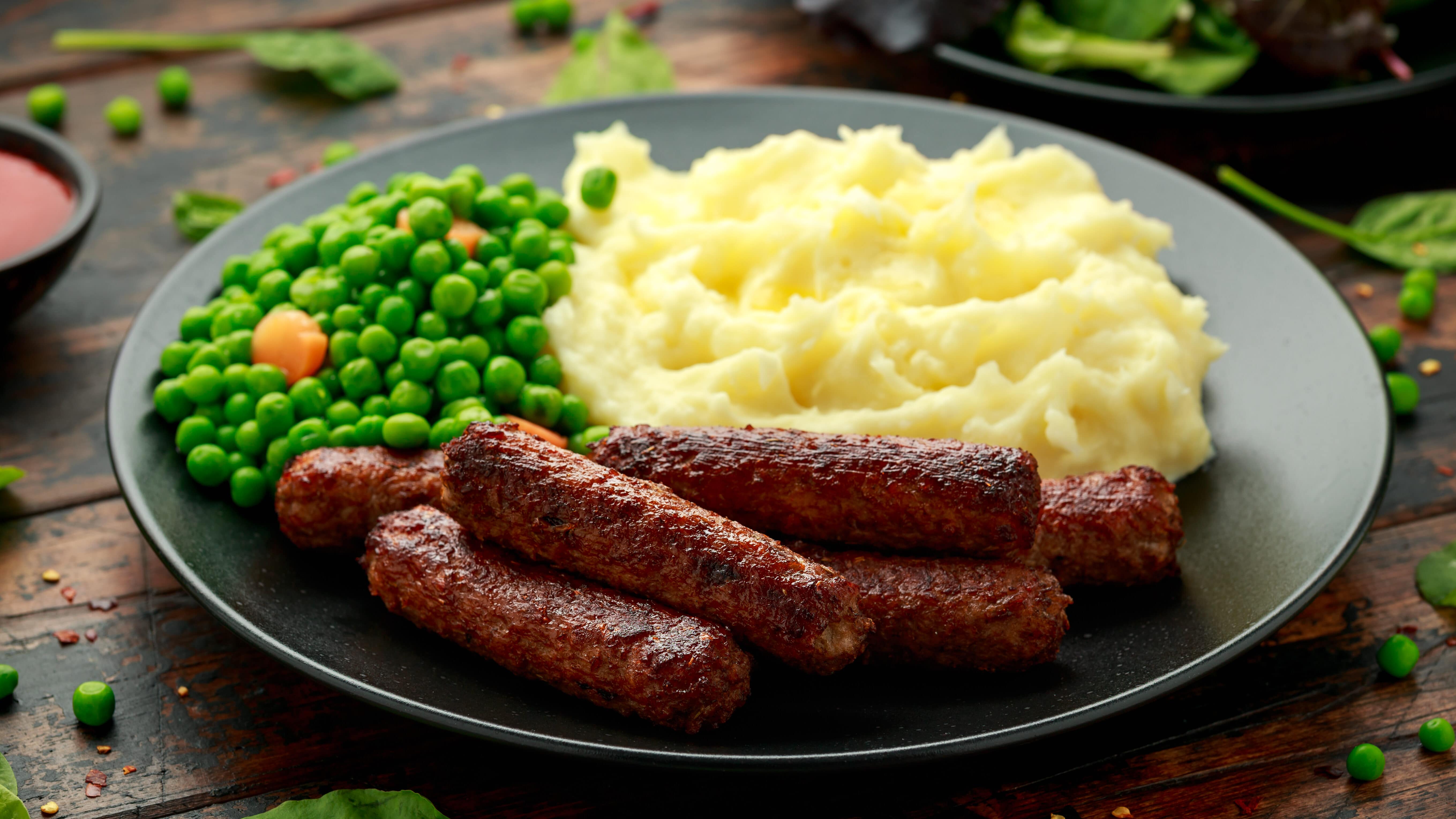 vegan sausages on a plate with mashed potatoes and cooked peas