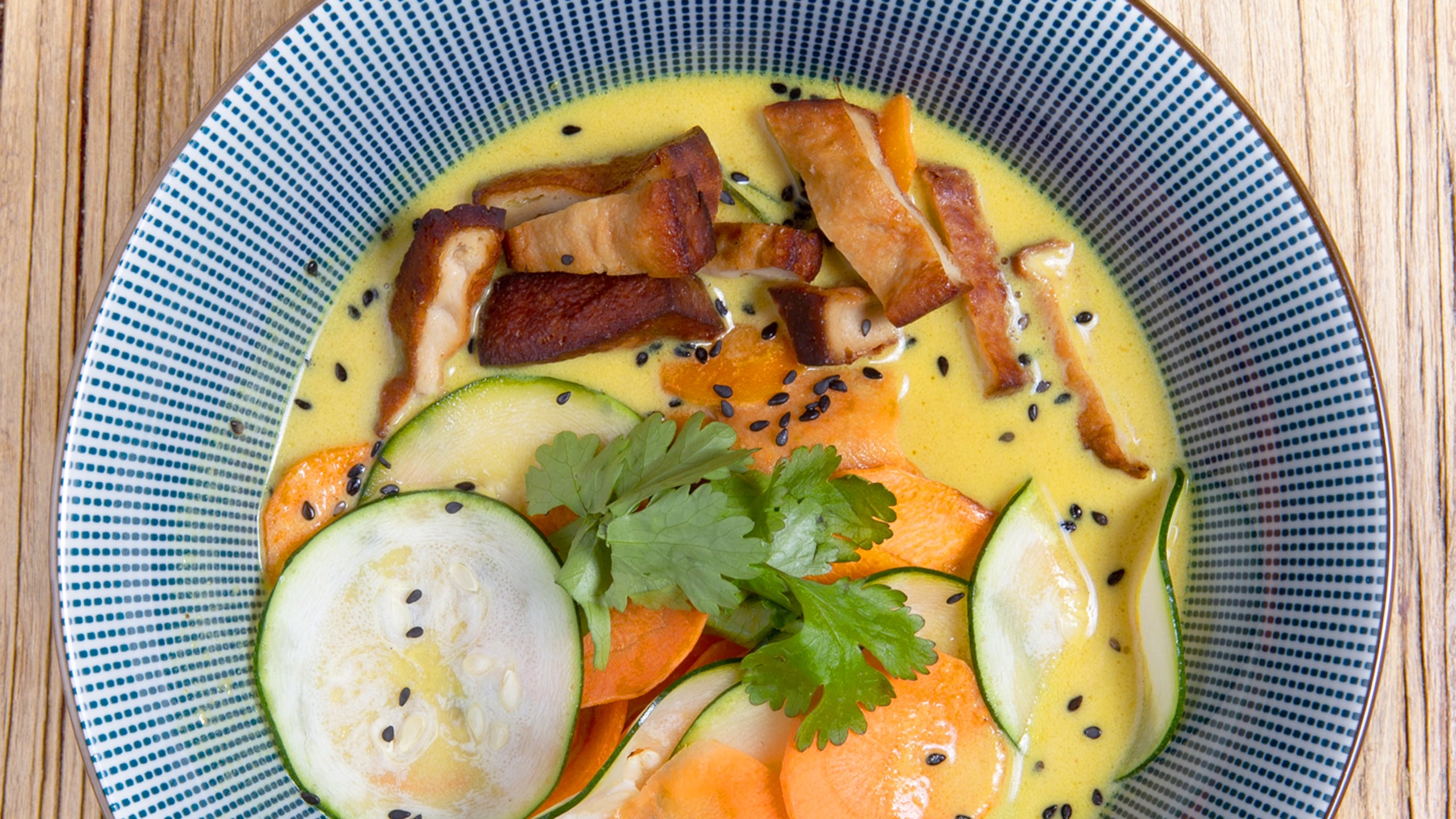 thick yellow cold soup with thin slices of raw vegetables and tofu