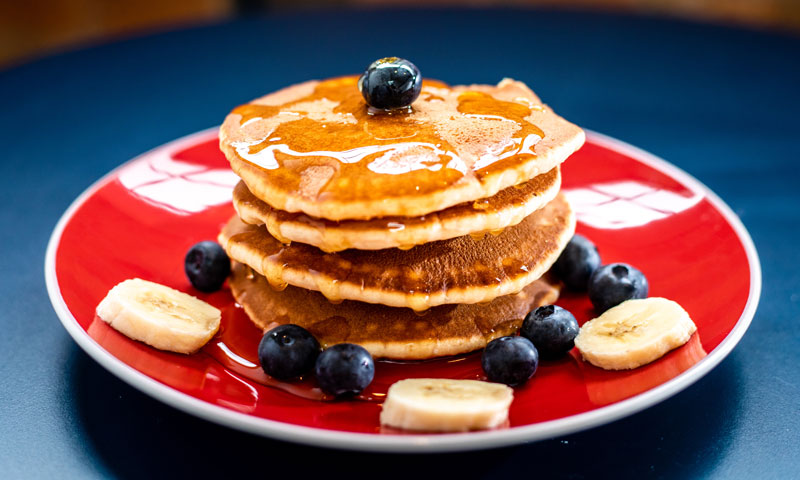 a pile of pancakes topped with maple, blueberries and banana slices