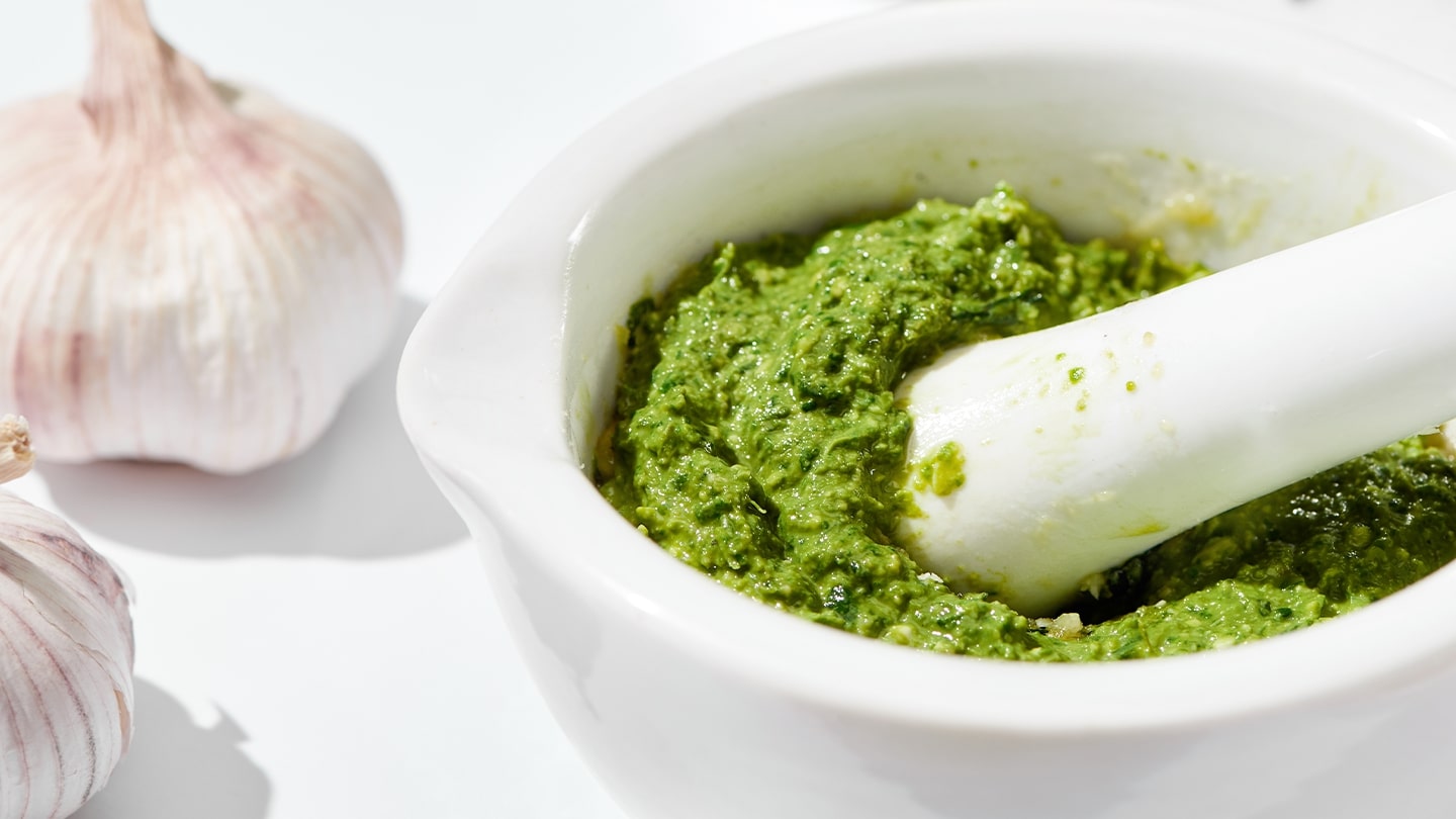 pesto dip inside mortar with pestle and garlic heads in the background