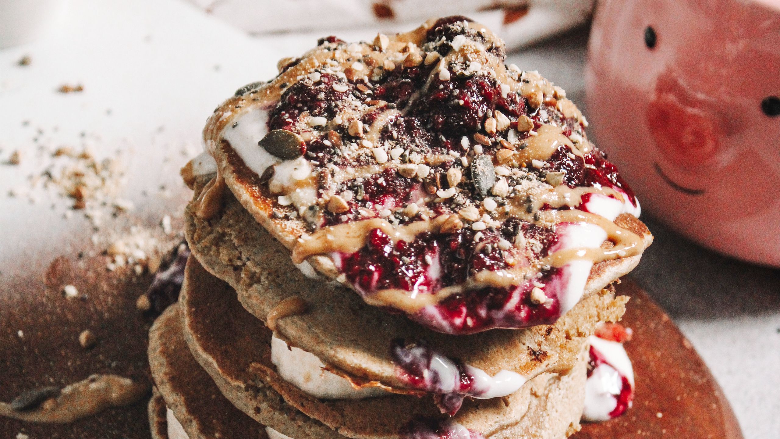 a pile of pancakes with toppings of sweet sauces and nuts