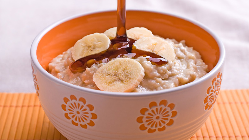 a bowl with oatmeal slices of bananas and maple syrup