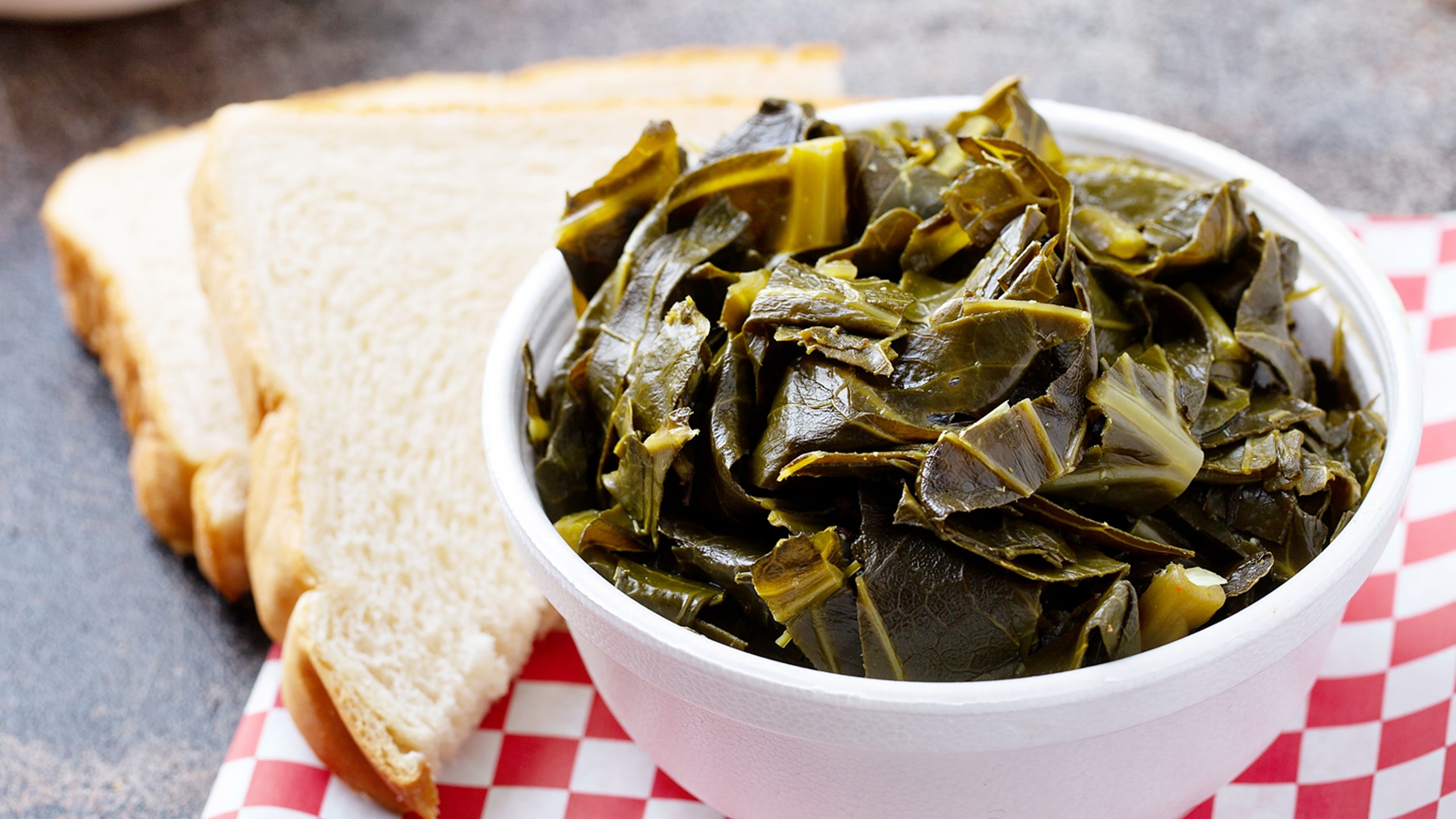 a bowl of cooked collard greens next to white bread slices