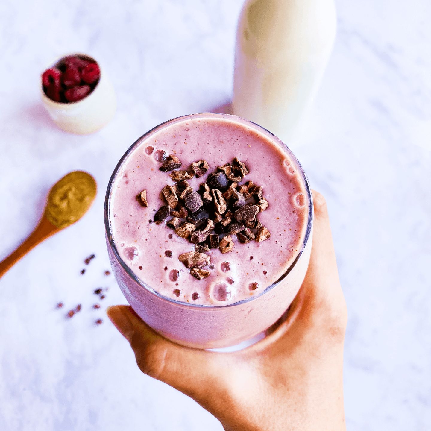 a hand holding a pink smoothie with cocoa nibs