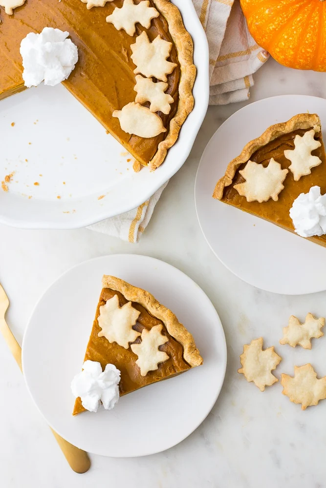 round pumpkin pie sliced with crusty leaf decorations and whipped cream