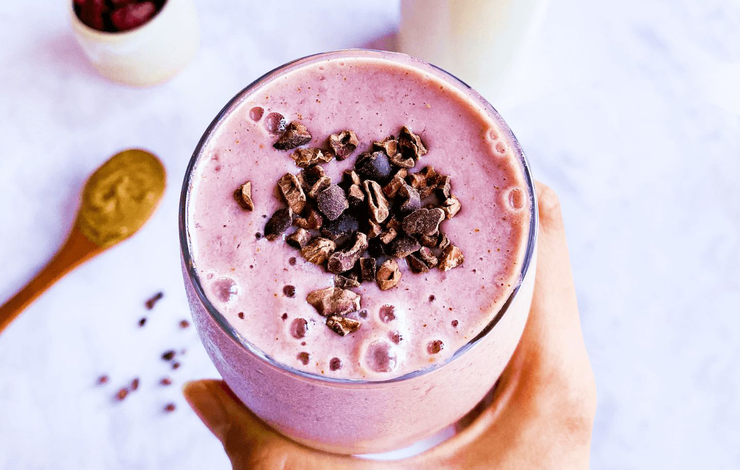 a hand holding a pink smoothie with cocoa nibs