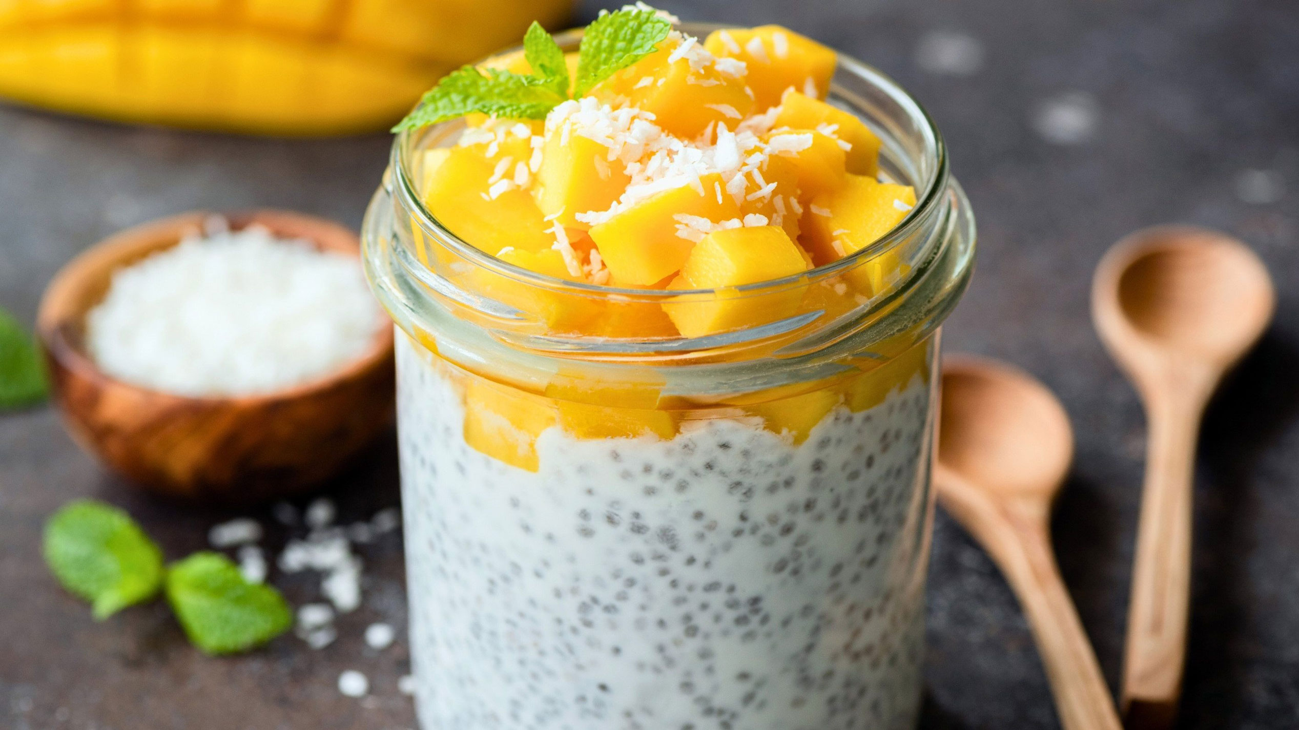 A clear jar filled with creamy chia pudding topped with mango cubes and a mint leaf for garnish