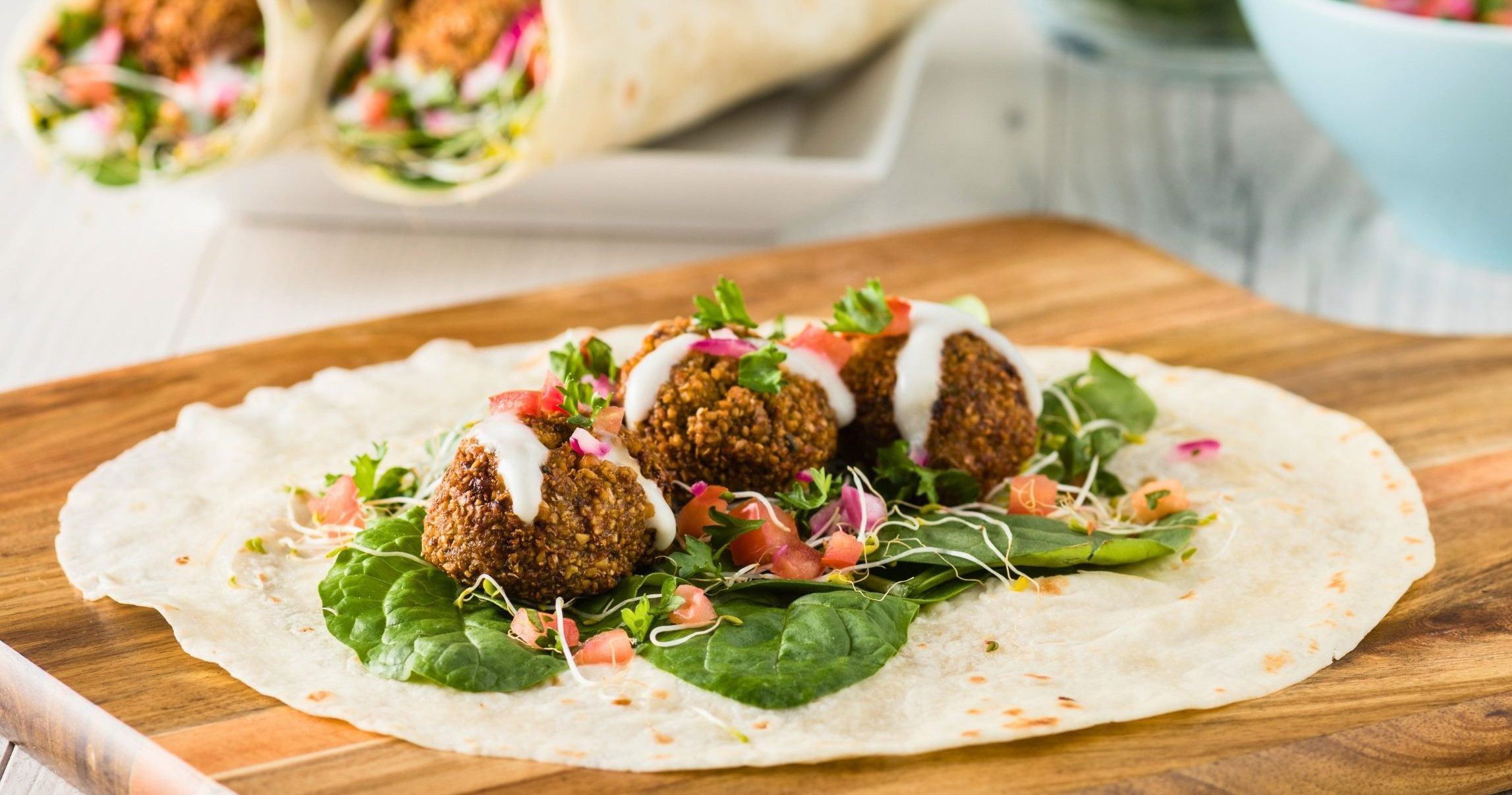 crunchy falafel balls on tortilla with fresh vegetables and a drizzle of tahini