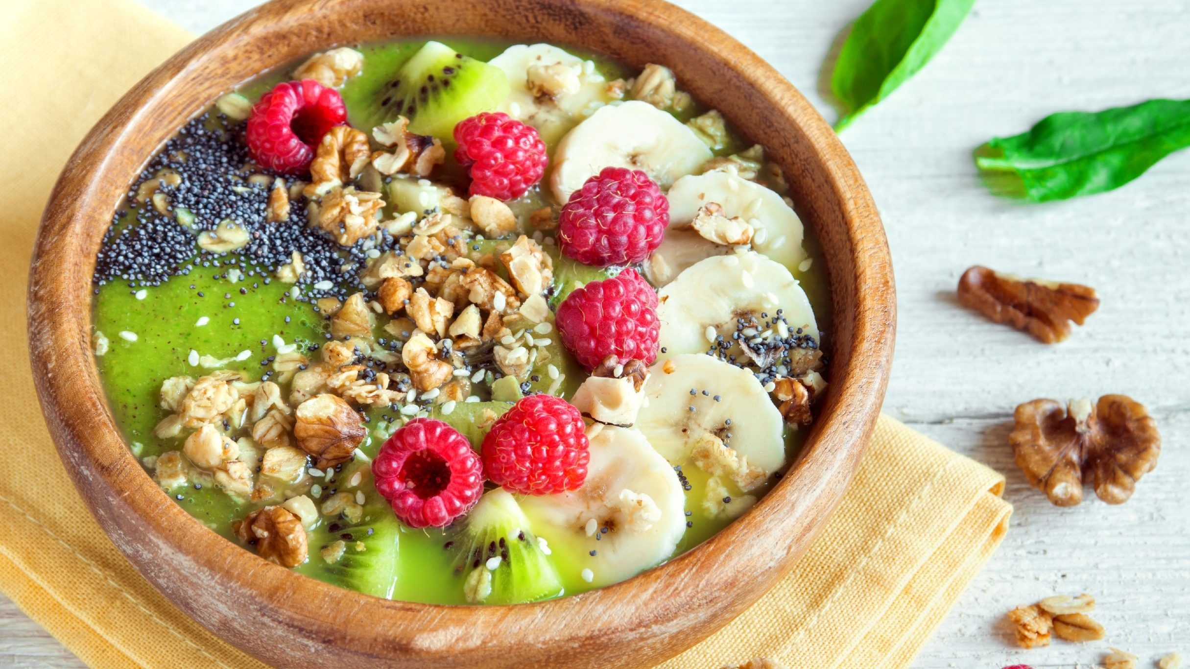 green smoothie bowl topped with fresh banana slices kiwi and raspberries and nuts and seeds