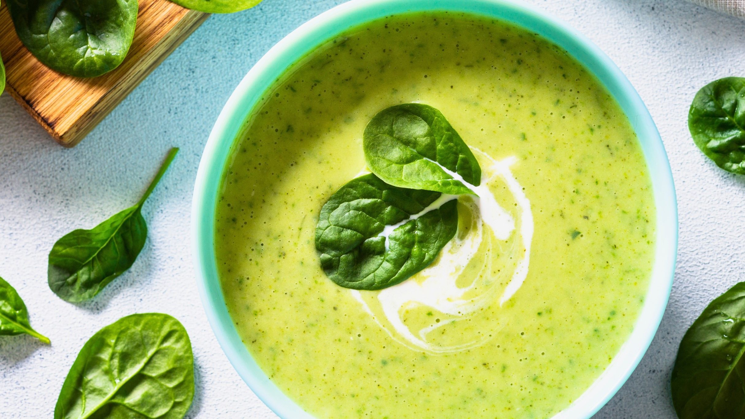 bowl of green soup with a splash of cream and spinach leaves for garnish