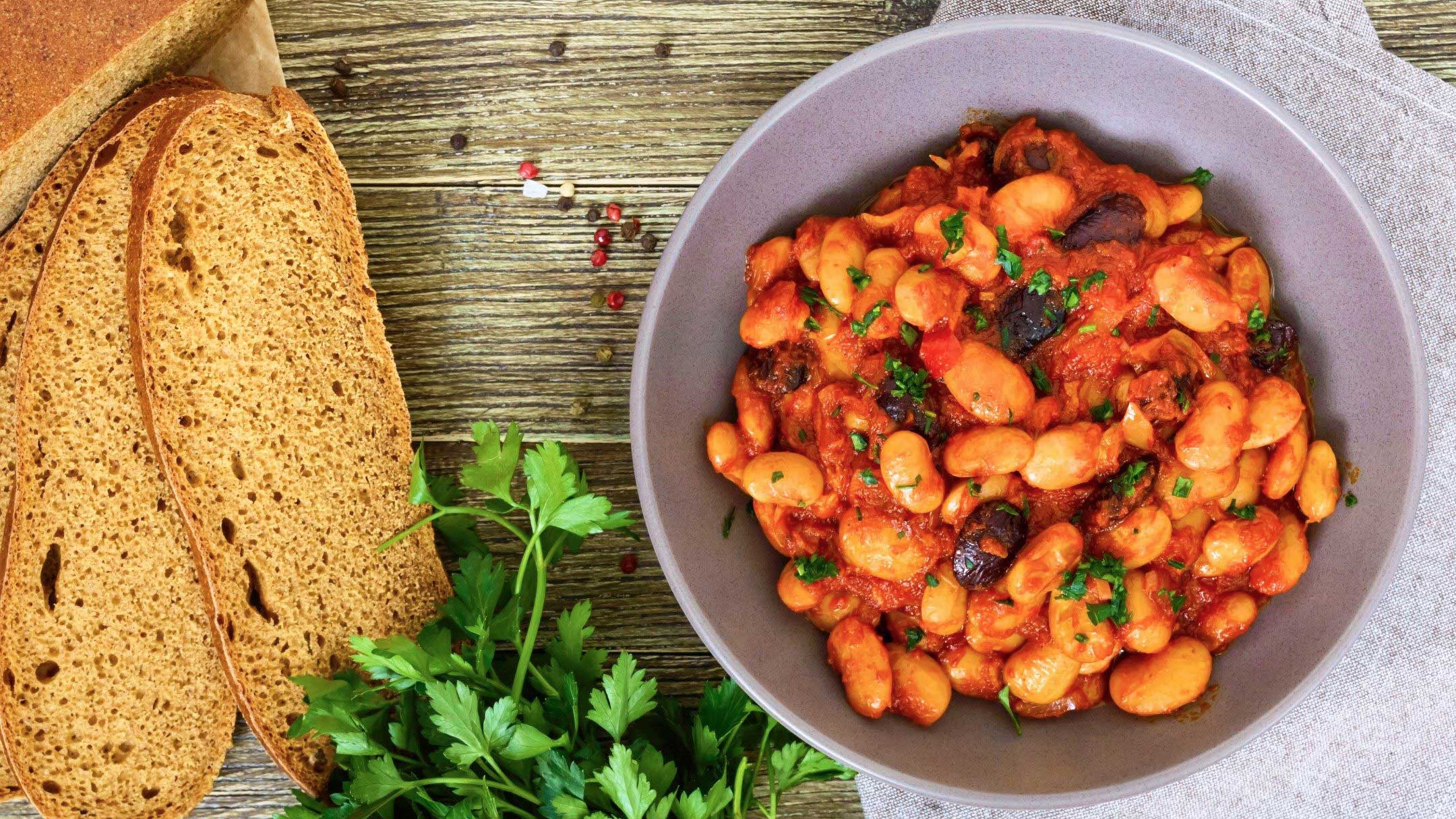 a bowl of bean stew in red sauce and two slices of bread next to it