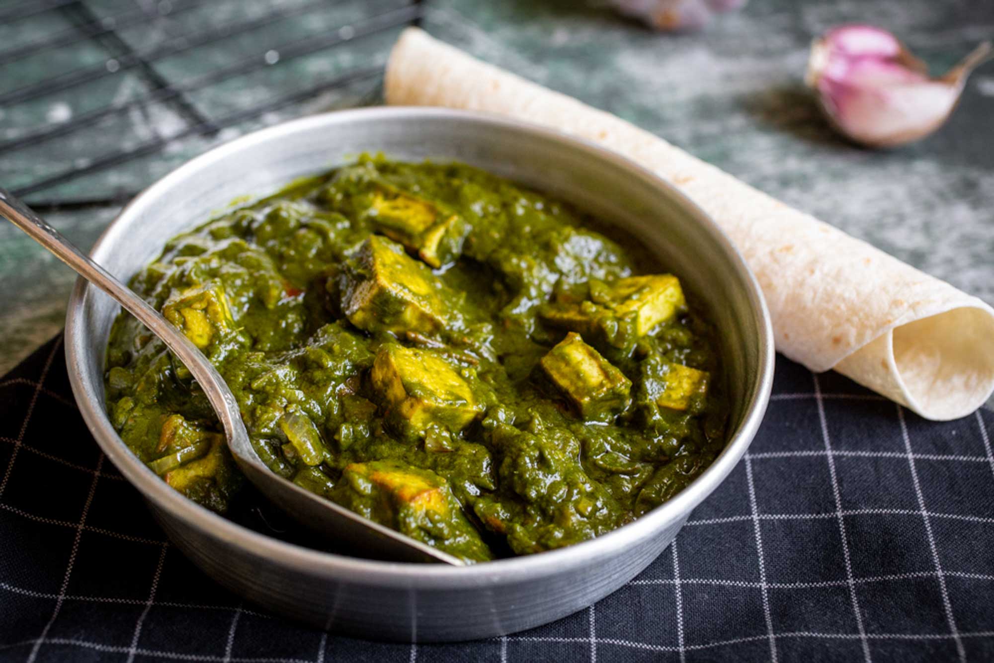 A pan of fresh vegan palak paneer made with tofu and spinach, with bread on the side